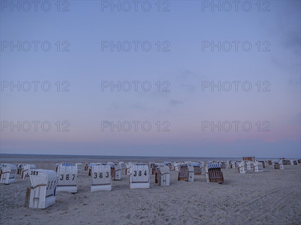 A quiet beach with white and striped beach chairs at dusk under a pastel-coloured sky, setting sun