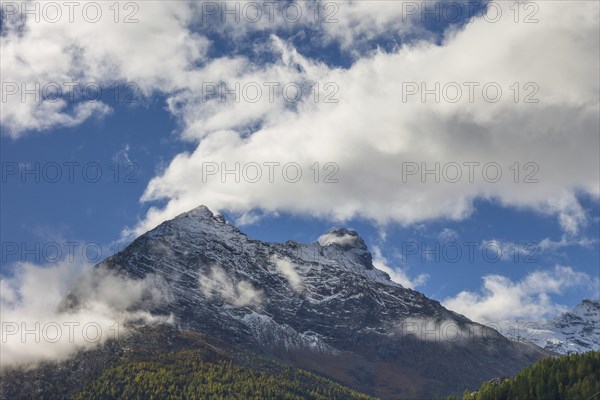 Snow covered mountain peak under a blue sky with scattered clouds, snow on high mountains in the