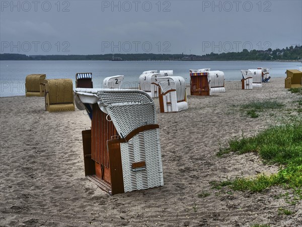 On the beach there are several beach chairs in different colours in front of a calm sea under a