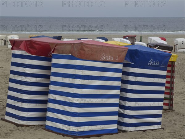 Several colourful beach chairs with stripe pattern standing on the beach in front of a cloudy sky,