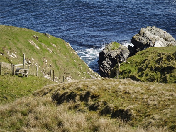 Cliffs and grassy hills on the coast overlooking the ocean, green meadows on a deep blue sea and a