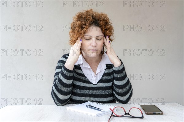 A mid-adult redhead woman with a headache is rubbing her temples