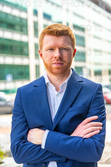 Vertical portrait of a confident young businessman looking at camera standing with arms crossed