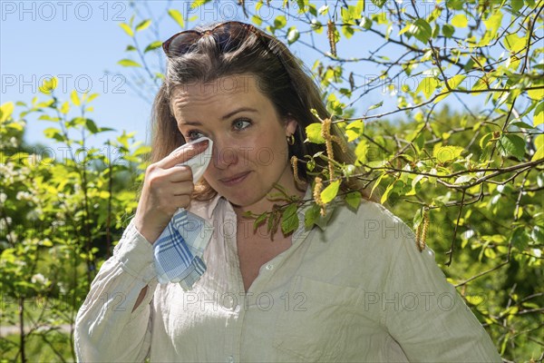 Young Caucasian woman, 35 years old, with allergy stands by flowering birch (Betula) in Ystad,