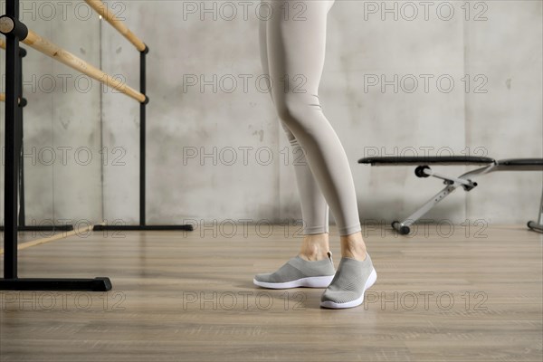 Slender female legs in sports leggings and sneakers near the handrail in the gym