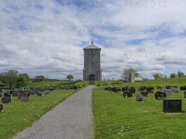 Stone church on a hill surrounded by a spacious cemetery with gravestones under a cloudy sky, old