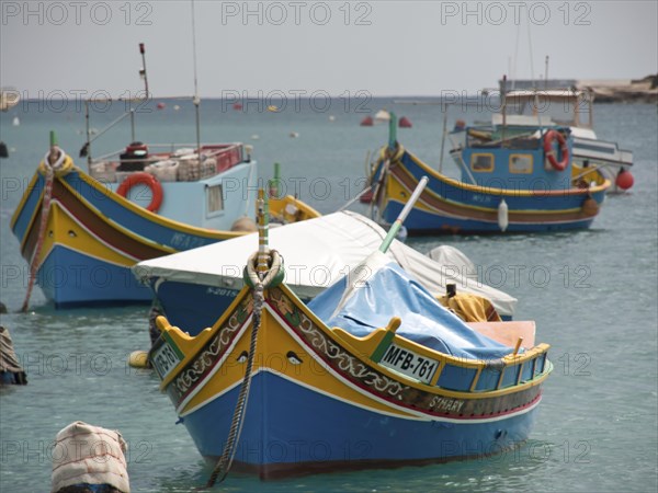 Several colourfully painted fishing boats anchor quietly in a harbour, surrounded by ropes and