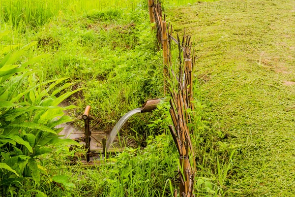 Water flowing from irrigation pipe spinning a small water wheel in canal in Chiang Khan, Thailand,