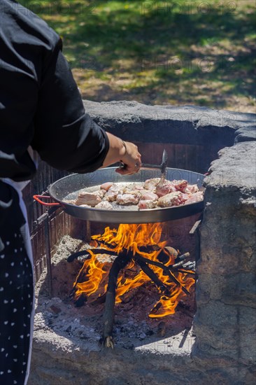Woman frying chicken in a paella pan on the fire in the countryside to make a typical spanish