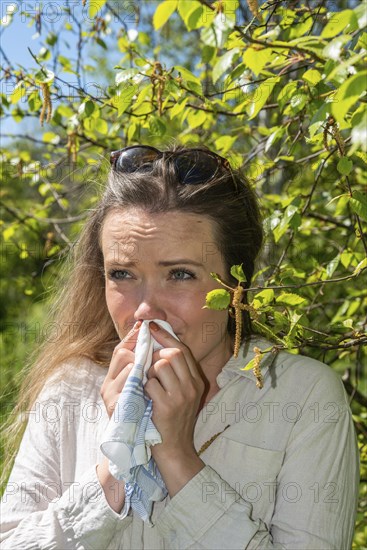 Young Caucasian woman, 35 years old, with allergy stands by flowering birch (Betula) in Ystad,