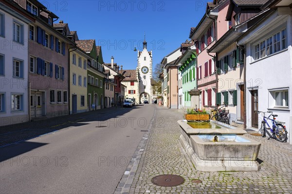 A picturesque old town street with colourful houses and a dominant clock tower under a clear blue