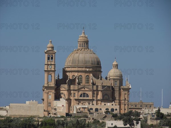 A large baroque basilica with a dome and detailed sandstone architecture set against a blue sky,