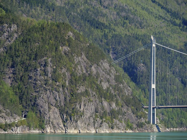 High bridge over turquoise water, surrounded by forested mountains and rocky cliffs, bridge in a
