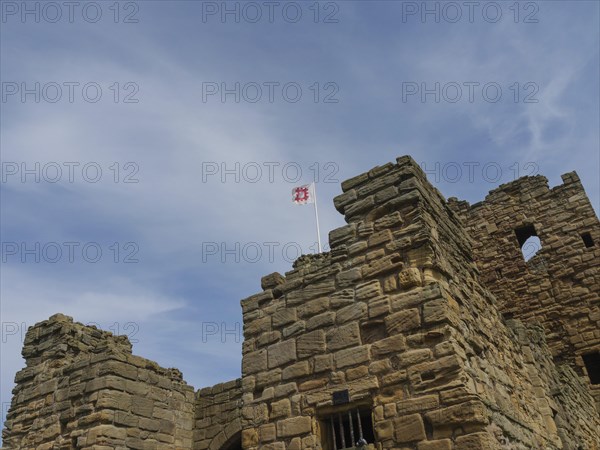 The top of a historic castle with stone towers and a waving flag under a cloudy sky, ruins and old