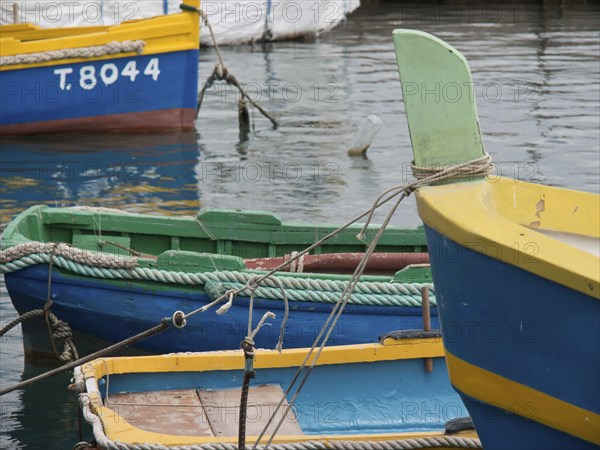 Colourful fishing boats moored in the clear water of the harbour with ropes, many colourful fishing