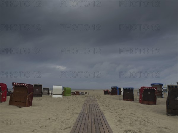 Dark clouds hanging over a beach with scattered beach chairs and a wooden jetty, beach chairs and