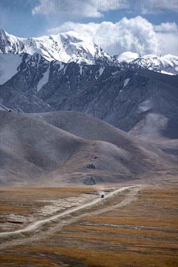 Car on a gravel track in the high mountain plateau, glaciated and snow-covered peaks, Ak Shyrak