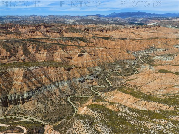 Extensive desert landscape with red rocks and canyons, criss-crossed by serpentines, aerial view,