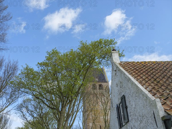 White house in front of a church with a tower, surrounded by trees under a blue sky, historic