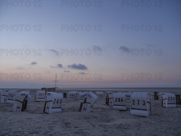 A calm dusk on a beach with white beach chairs and a soft sky, setting sun on a beach with beach