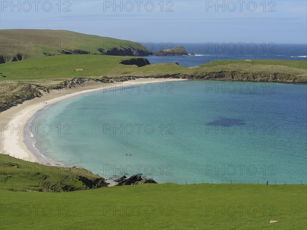 A scenic panorama with a wide, peaceful sandy beach surrounded by green meadows and turquoise blue