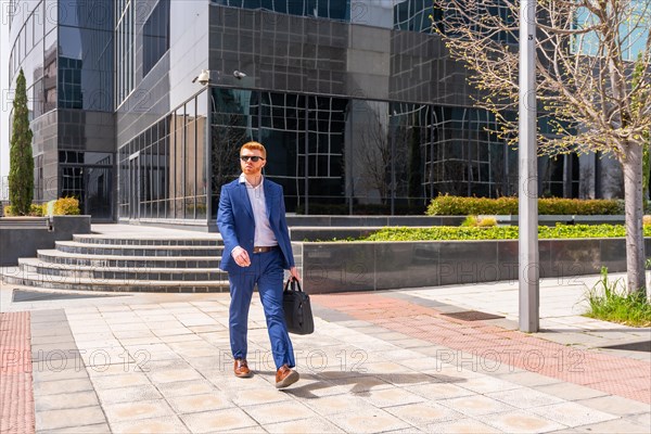 Businessman carrying laptop bag walking along city next to financial building
