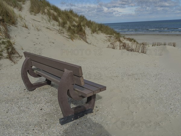 Beach scene with a wooden bench, dunes and sea under a cloudy sky, dunes on an island with a blue