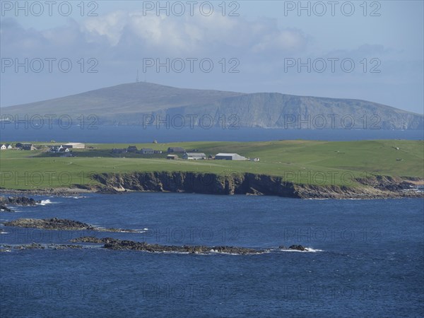 Green fields stretch to the jagged cliffs in front of the deep blue sea and a distant island, green