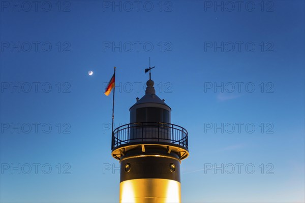 Black and white lighthouse, called 'Kleiner Preusse', stands illuminated at night shortly after