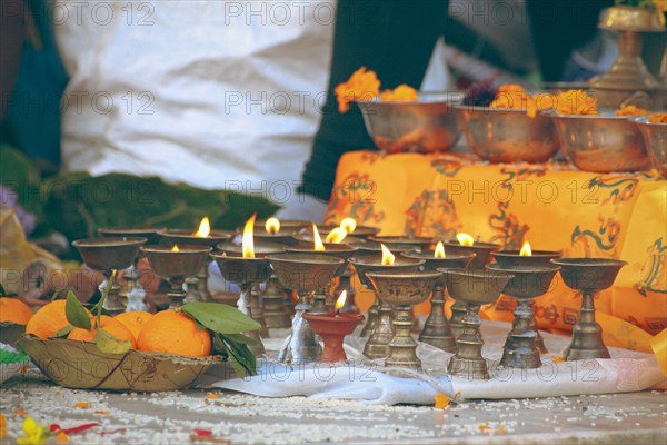 Close up to lit brass ghee lamps or butter lamps and sacred marigold flowers offering during