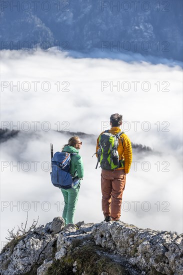 Two hikers at Ettaler Manndl, view over mountain landscape and sea of clouds, high fog in the