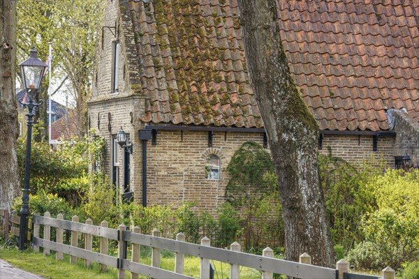 Historic house with brick wall, fence and street lamp, surrounded by trees and a garden, historic