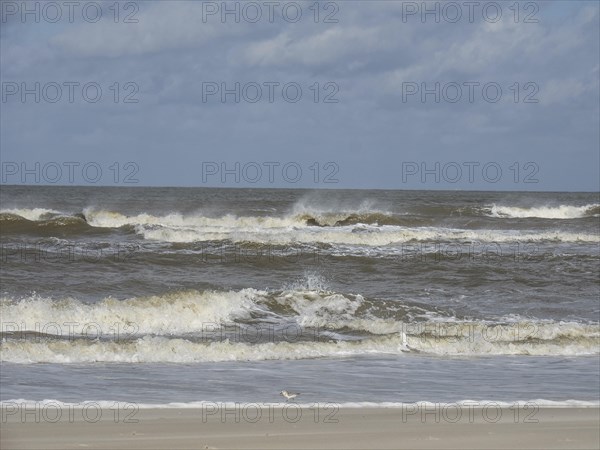 Interwoven waves with whitecaps on the seashore under a cloudy sky, waves on a beach, sunny day