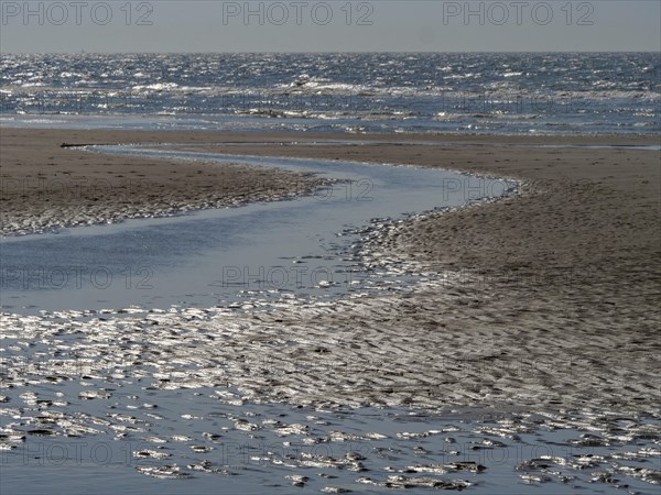 Beach with a gently curving watercourse in the sand and blue sea in the background, glittering sea