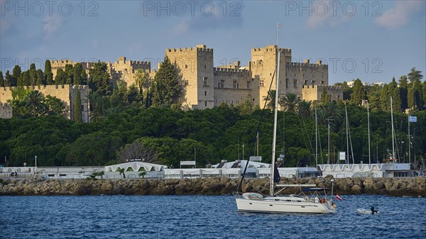 Historic castle by the sea with yacht in the foreground and cloudy sky, trees, Grand Master's