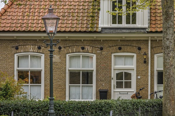 An old brick house with white windows and a lamppost in the foreground, old houses with green