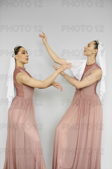 Two beautiful ballerinas practicing in front of each other over grey wall