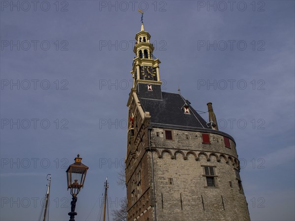 Historic stone clock tower against a sky blue background with an antique lamp in the foreground,