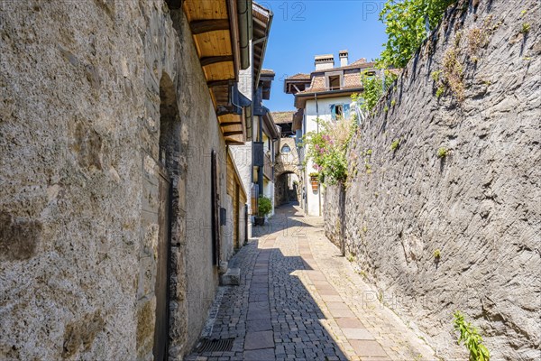 Narrow alley with cobblestone alleyway and old buildings, surrounded by stone walls and flowers,