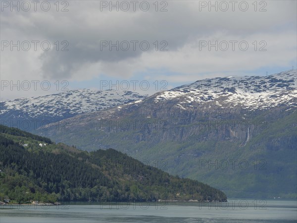 Impressive landscape with snow-capped mountains, a lake and forest under a slightly cloudy sky,