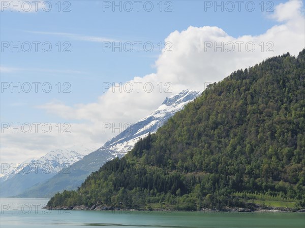 Green mountain slopes with snow-covered peaks and a lake under a slightly cloudy sky, greenish
