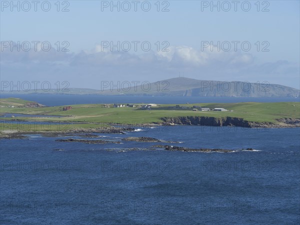 View of the azure blue sea, where green fields reach to the rocky coast, green meadows on a deep