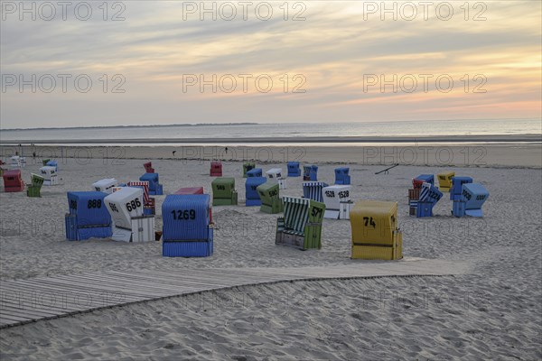 Atmospheric evening sun on a quiet beach with colourful beach chairs and a wooden walkway in the
