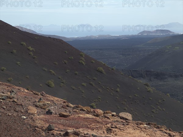 An overgrown volcanic hill with a view of the distant sea under a slightly cloudy sky, barren