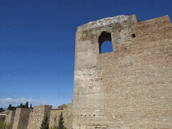 High stone tower with window opening surrounded by blue sky and sunlight, stone walls of an old