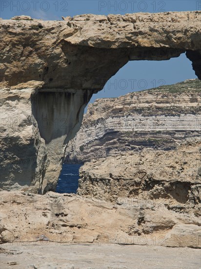 Natural rock arch on the coast, surrounded by rocks and sea under a blue sky, many historic