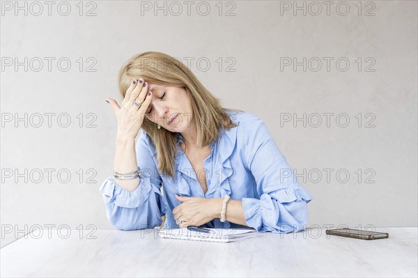A mid-adult blonde woman is holding one hand on her forehead