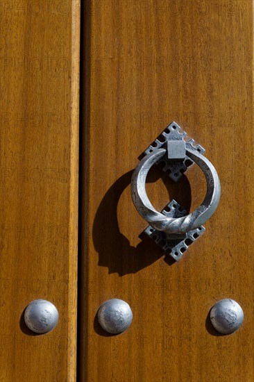 Latch on a wooden door with metal rivets illuminated by sunlight with shadows