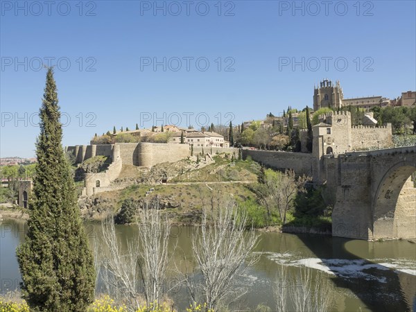Historic fortress with walls and cypress trees on a hill with river in the foreground on a sunny