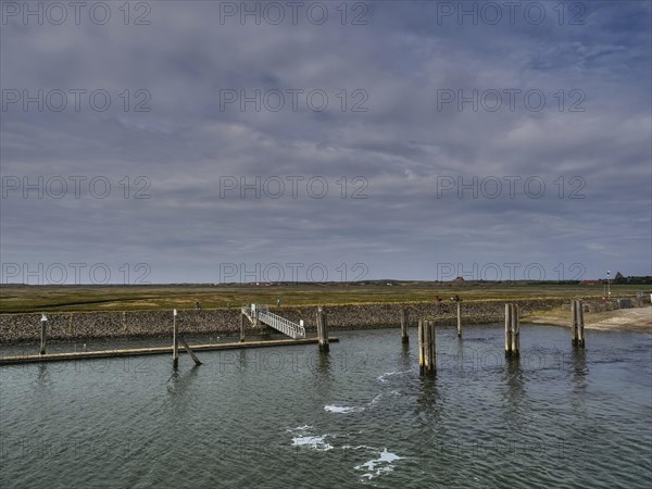 A long jetty in the sea with a cloudy sky and coastal landscape in the background, small jetty with